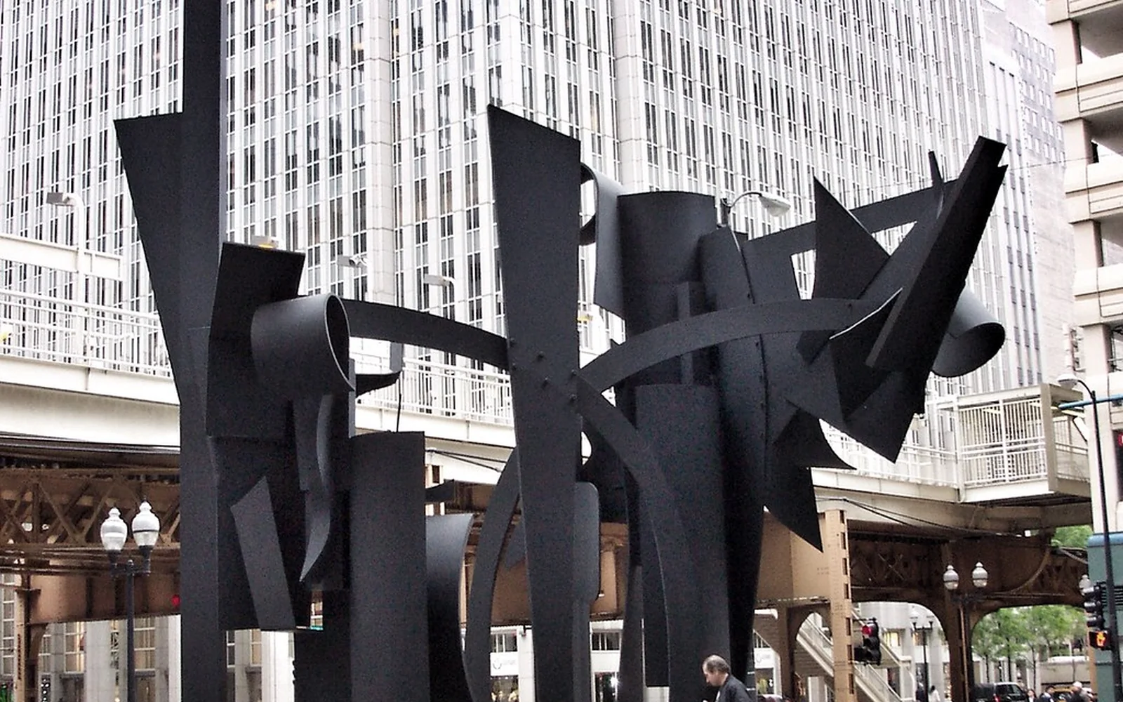 Escultura abstracta de acero instalada en una plaza entre edificios.