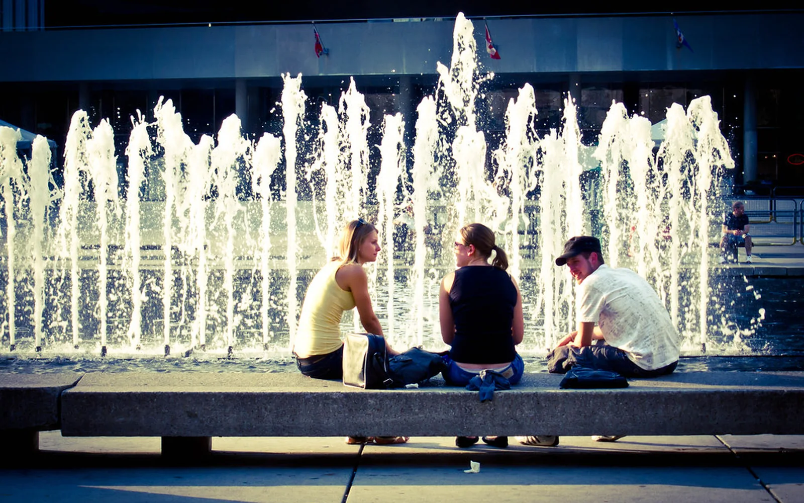 Tres personas conversan sentadas junto a una fuente urbana.