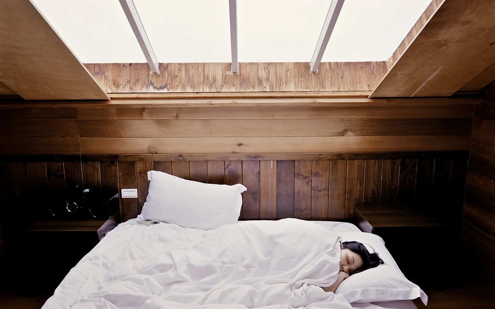 Dormitorio de madera con una cama preparada bajo una ventana.