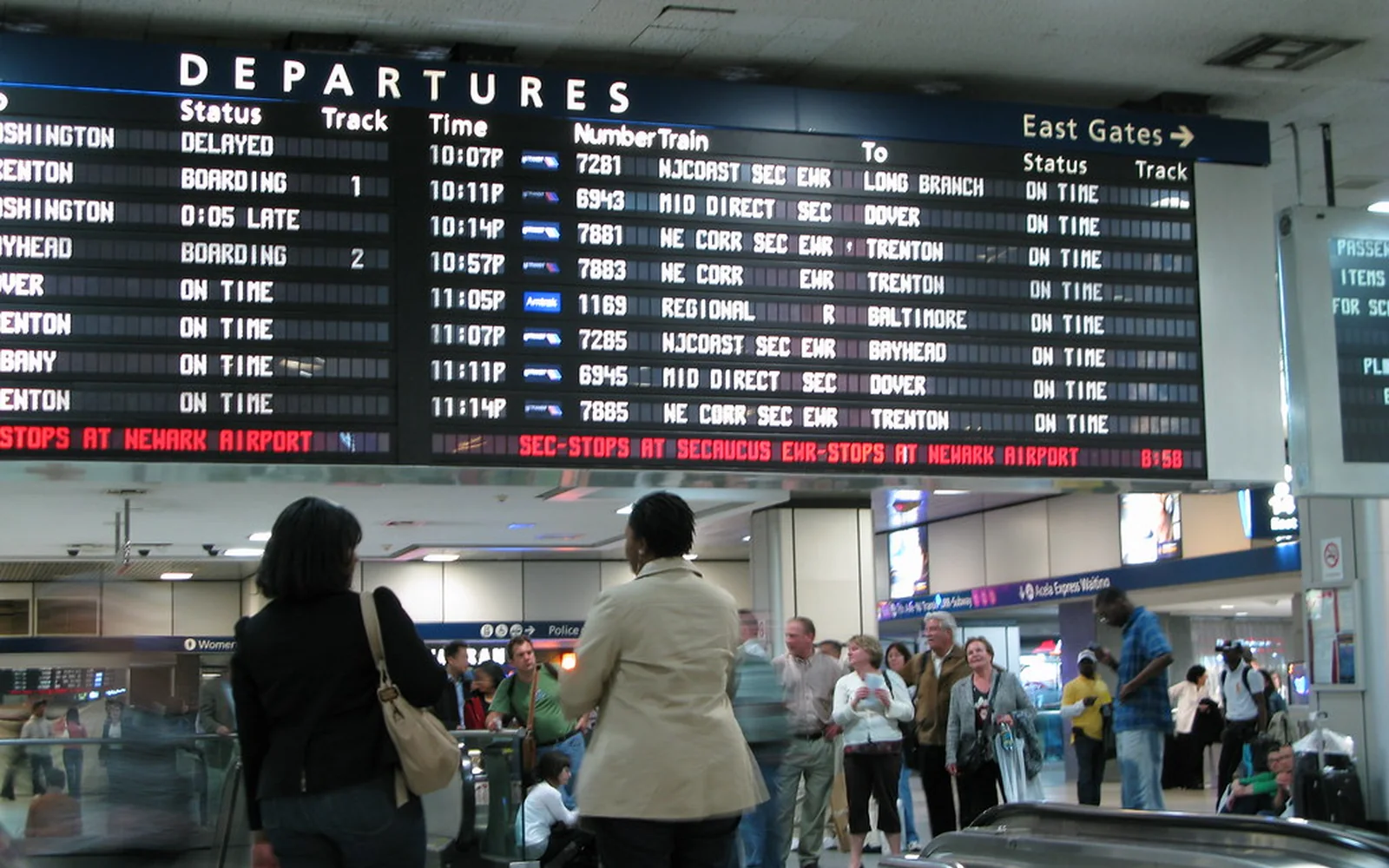 Viajeros esperan bajo el panel de salidas de una estación.