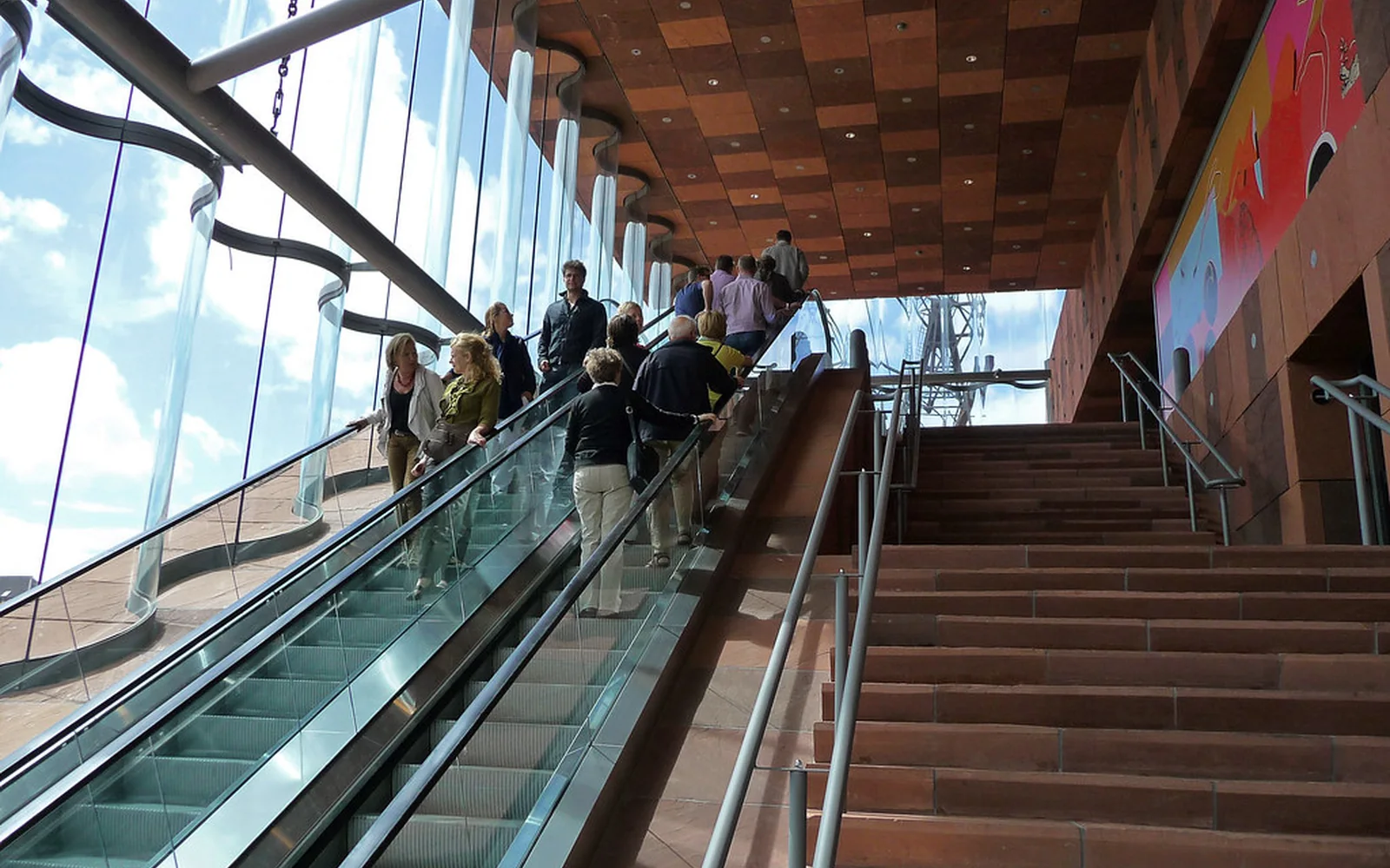Visitantes ascienden por las escaleras mecánicas de un museo contemporáneo.