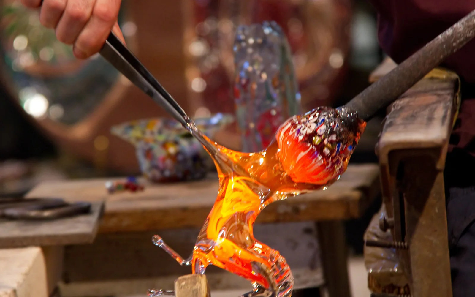 Una artesana trabaja vidrio fundido de color naranja con herramientas manuales.