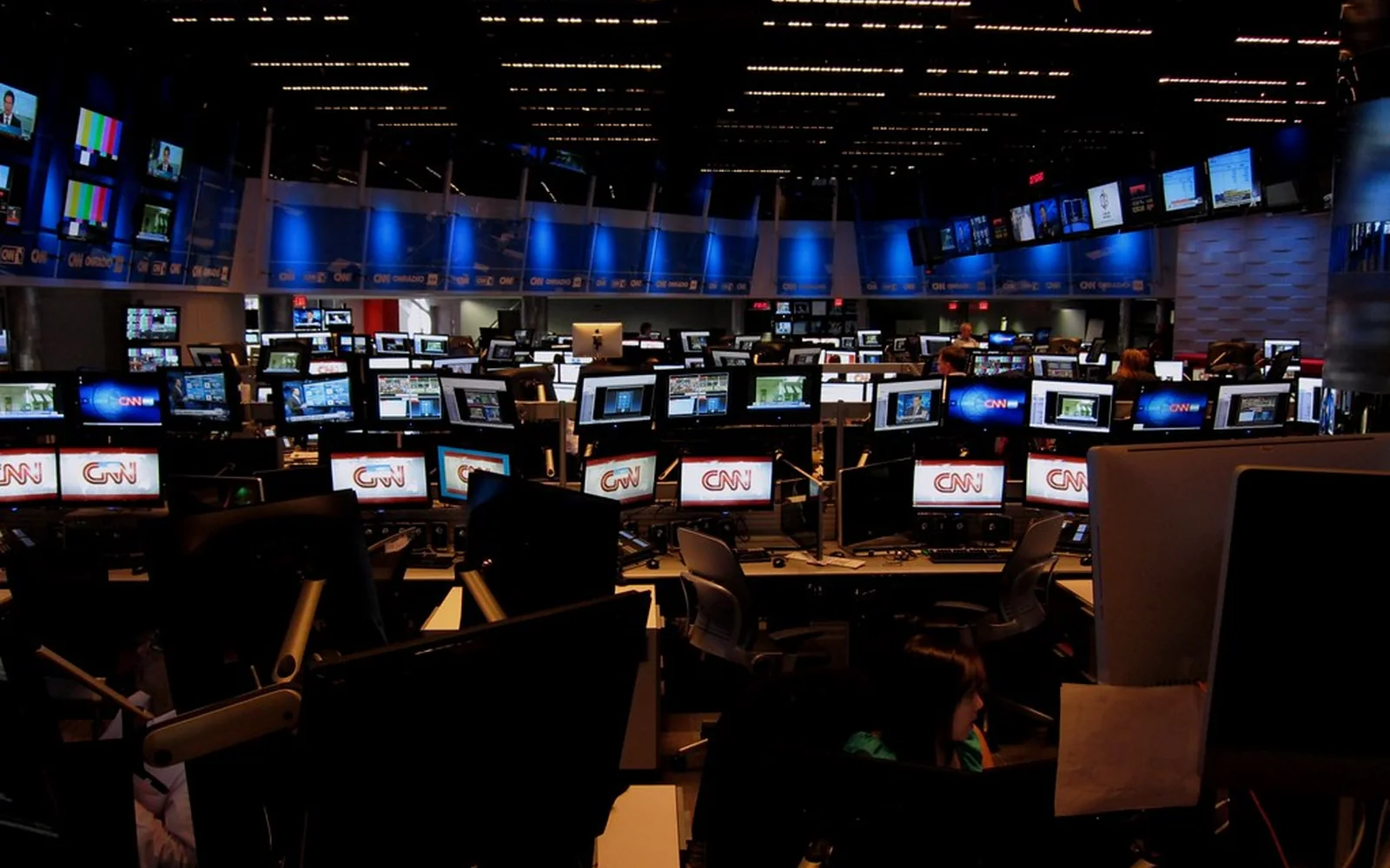 Sala de control de un canal informativo con numerosos monitores encendidos.