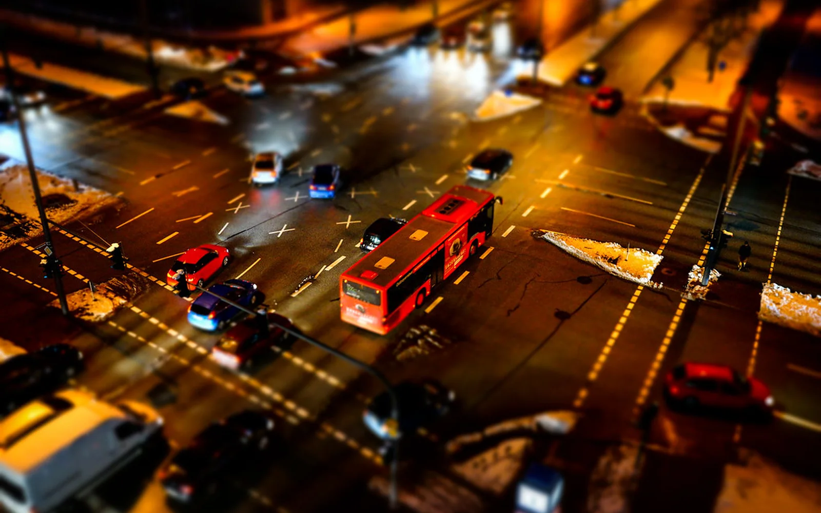 Cruce urbano iluminado de noche con coches y autobuses en circulación.