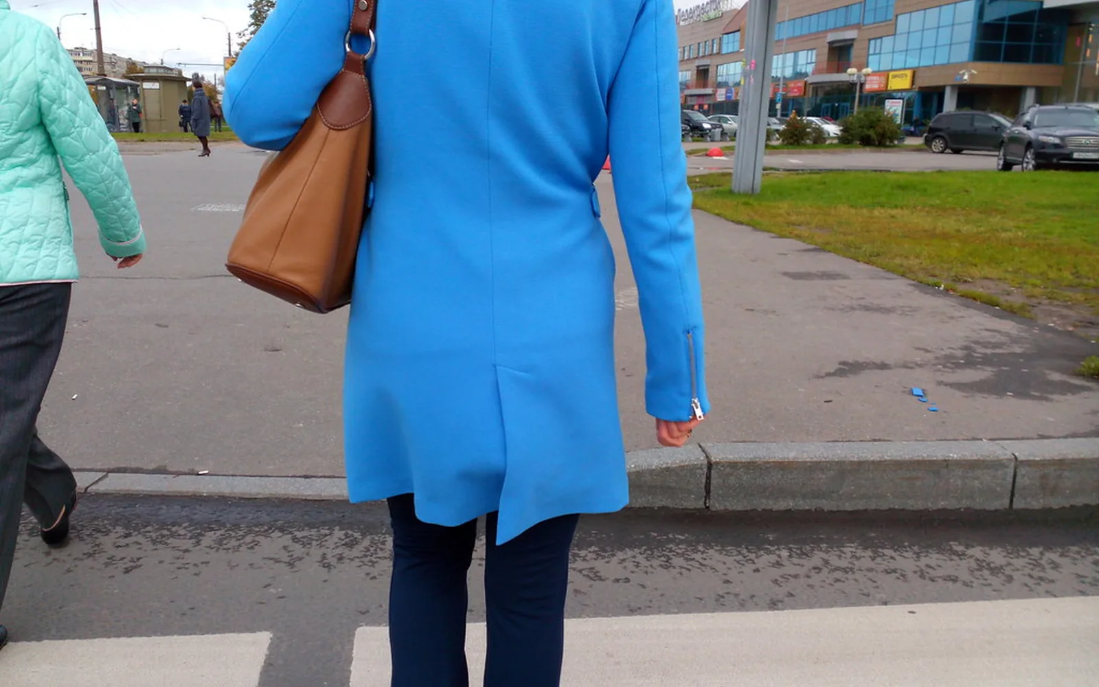 Una mujer con abrigo azul camina tranquilamente por una acera.